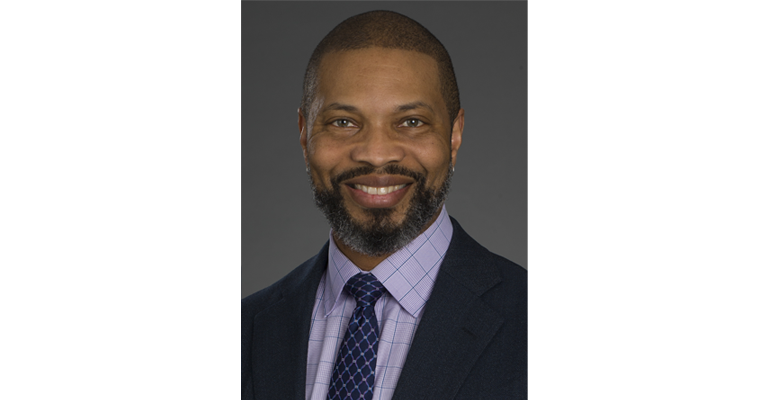 Turahn Dorsey smiles at the camera wearing a suit jacket and tie