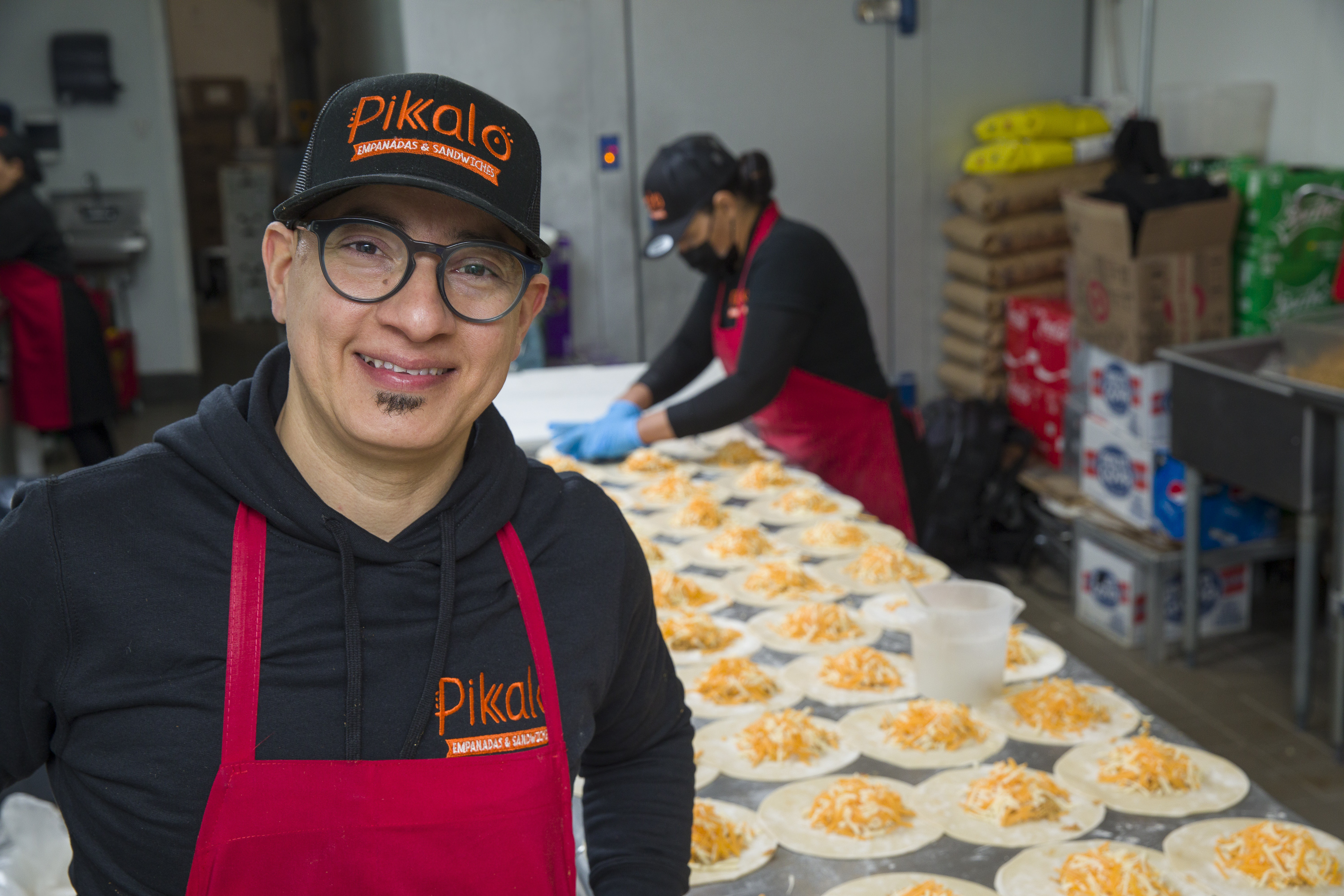 Jose Pimental, owner of Pikalo, stands in kitchen in front of table filled with empanadas