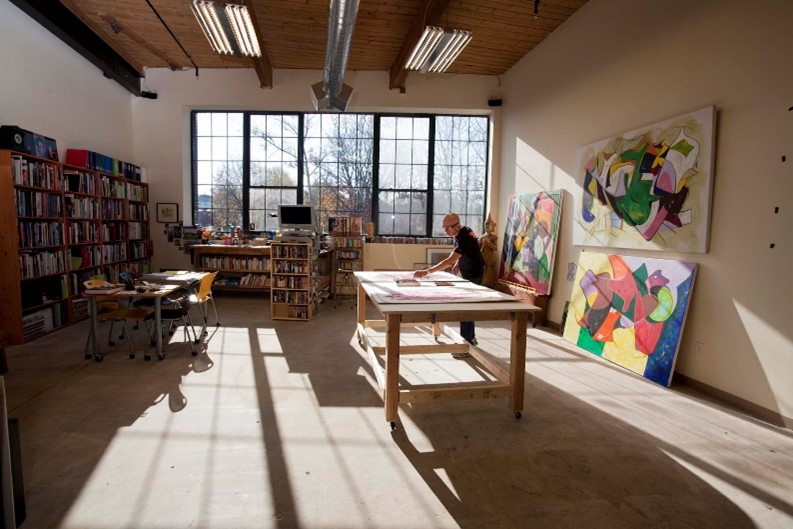 A man making art at a large wooden table in a large art studio