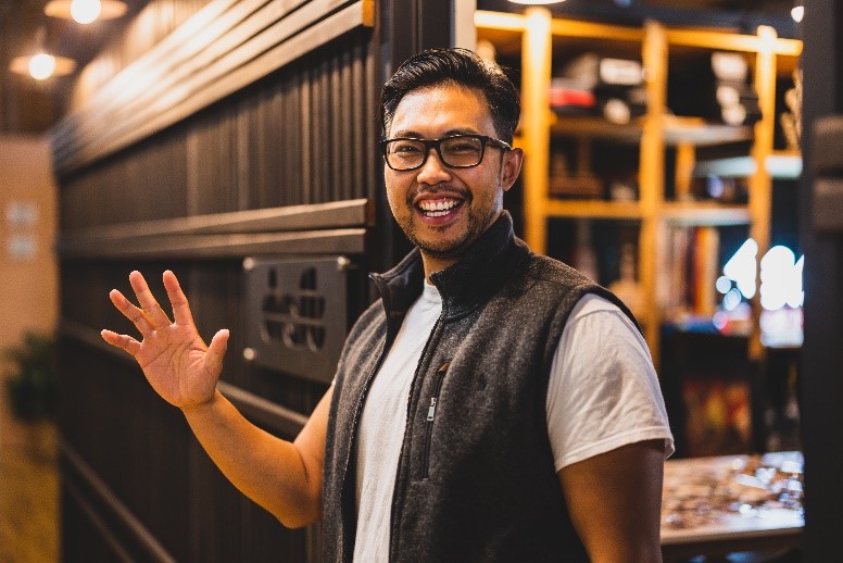 A man smiles and wave to the camera