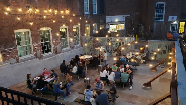 People sitting at picnic tables on a cement patio outside of brick building
