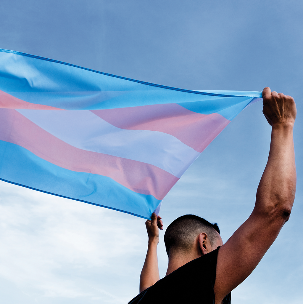 A man proudly holds the transgender flag over his head