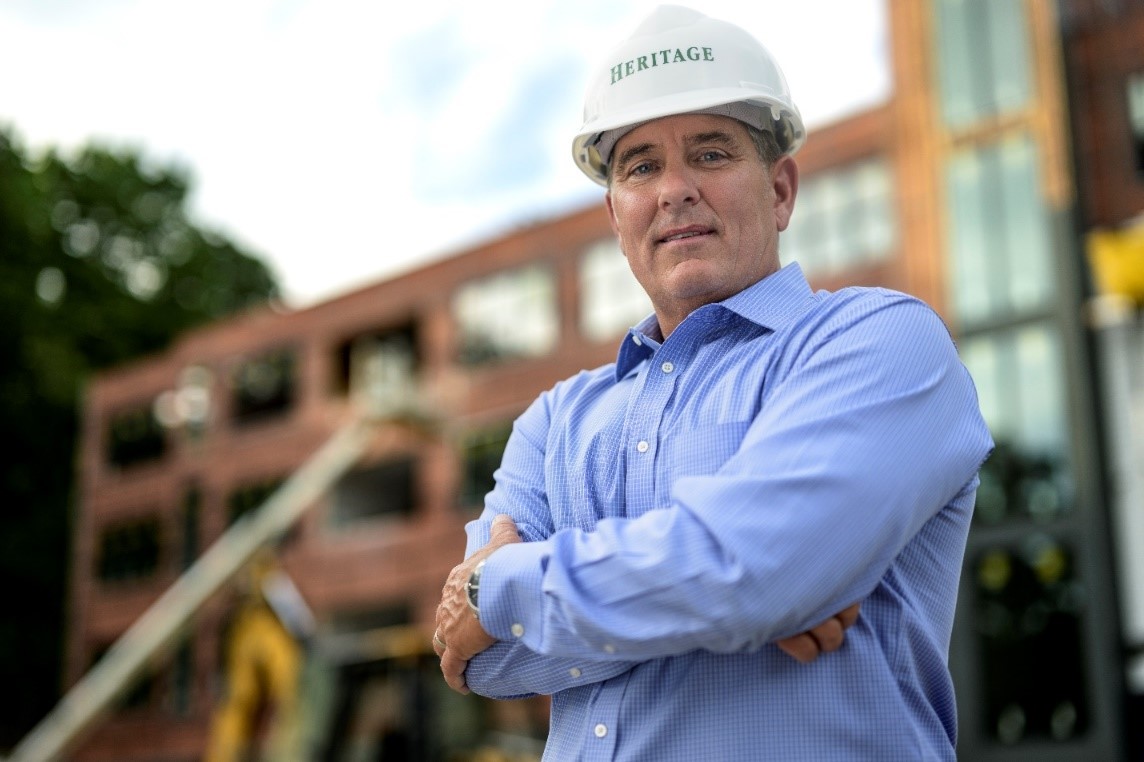 Heritage Companies president Michael Kiley wears a construction hat while standing outside of a building under construction