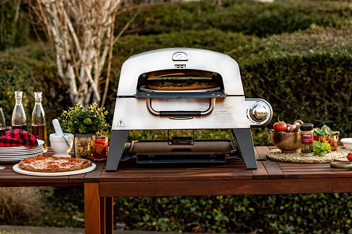 A portable outdoor pizza over sits on top of a wooden picnic table