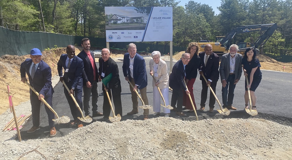 Employees of LeClair Village Apartments dig dirt from a pile of gravel in front of their construction site and smile for the camera