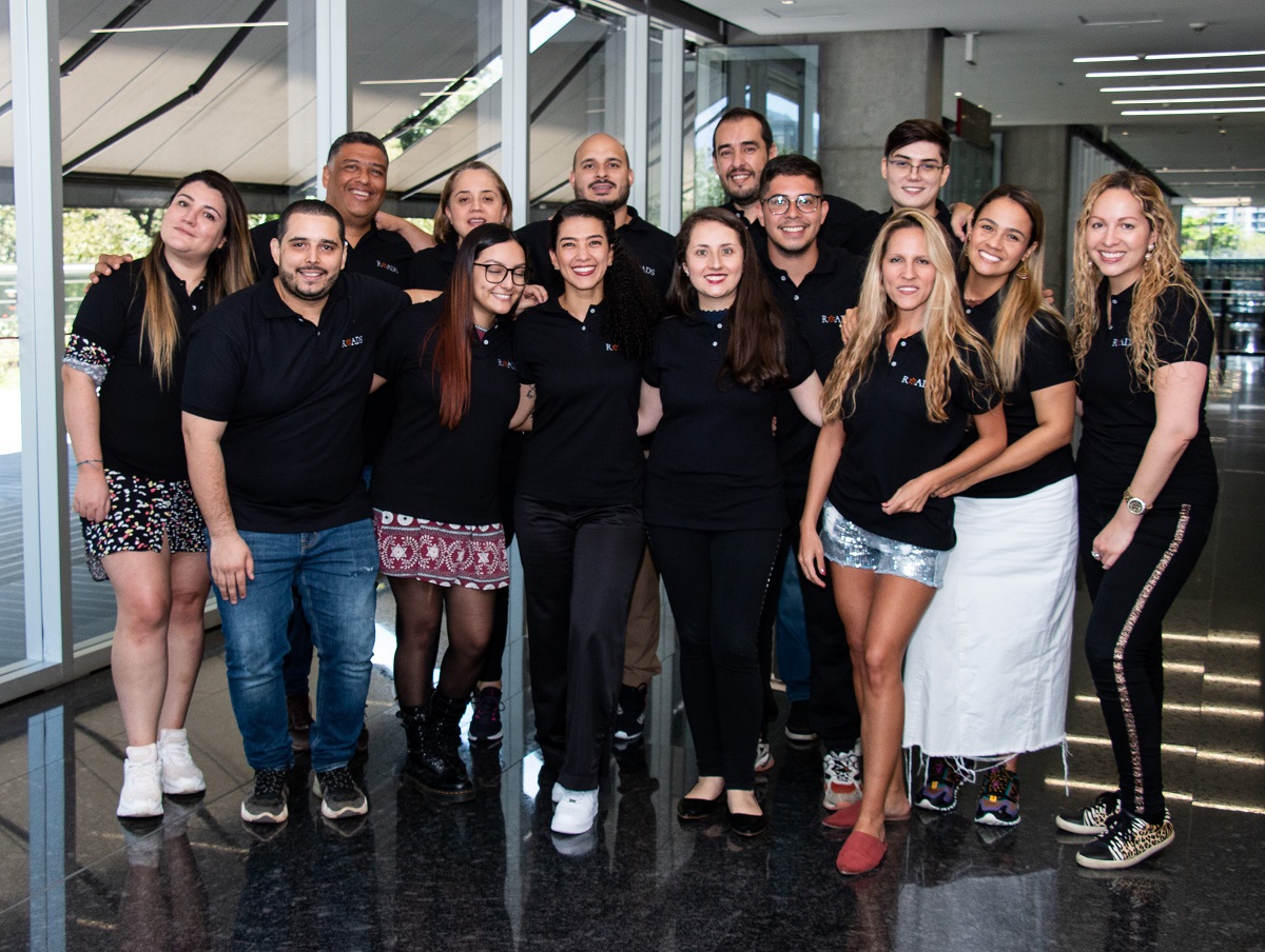 Roads Consulting Group team members stand together in branded black polo shirts and smile at the camera