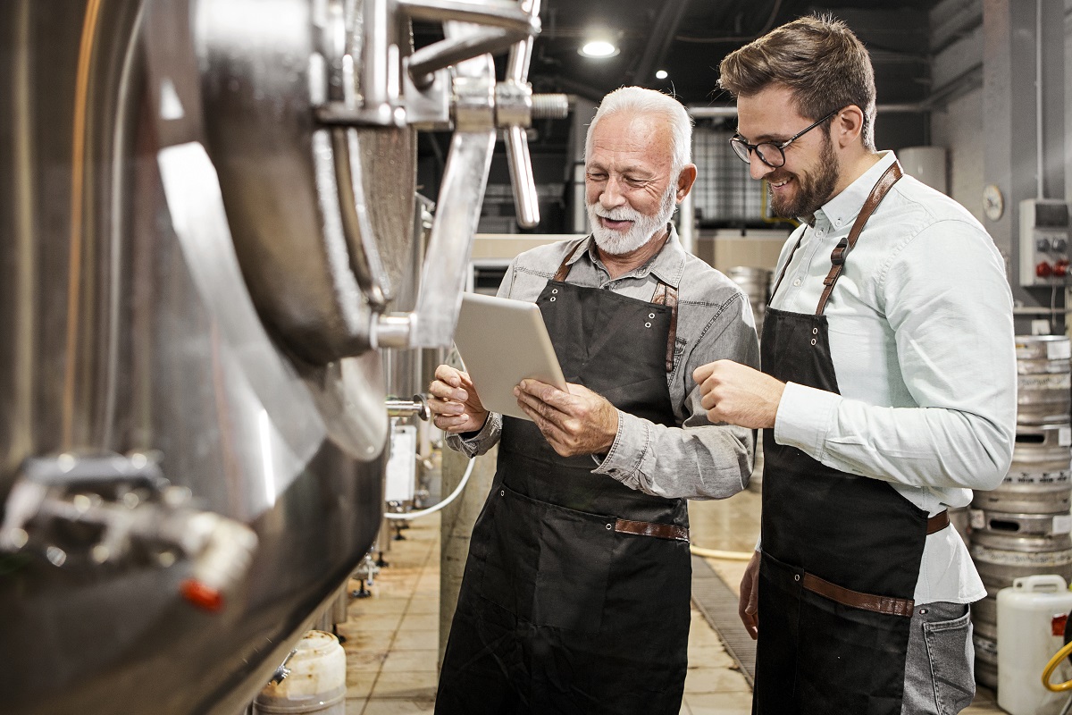 A father and son wear aprons as they meet in their brewery's tap room to review inventory