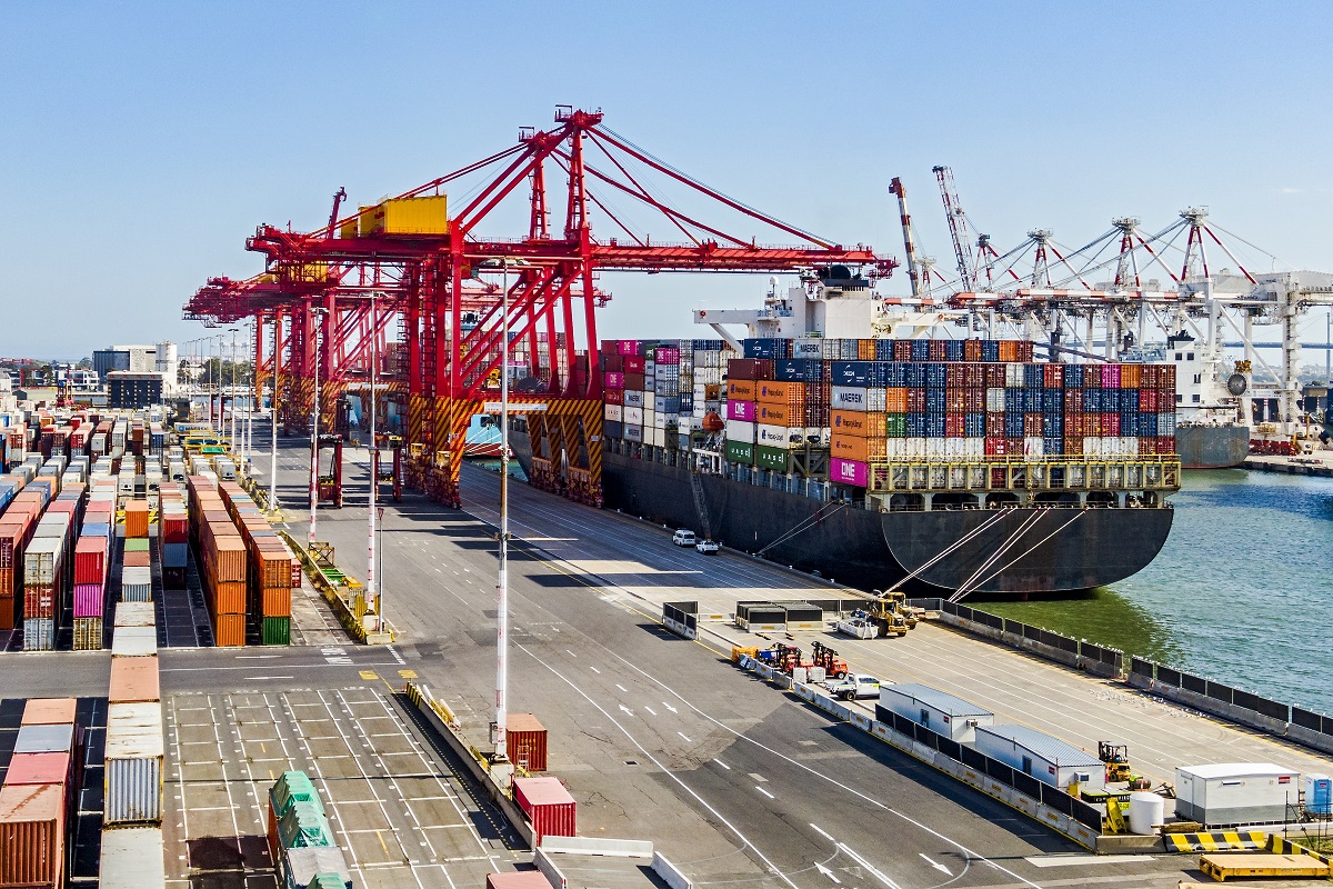A photography view of a dock in a wharf with a large cargo ship stacked with shipping containers