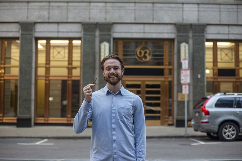 Connor Schoen stands in front of a building in Boston and holds up the building key