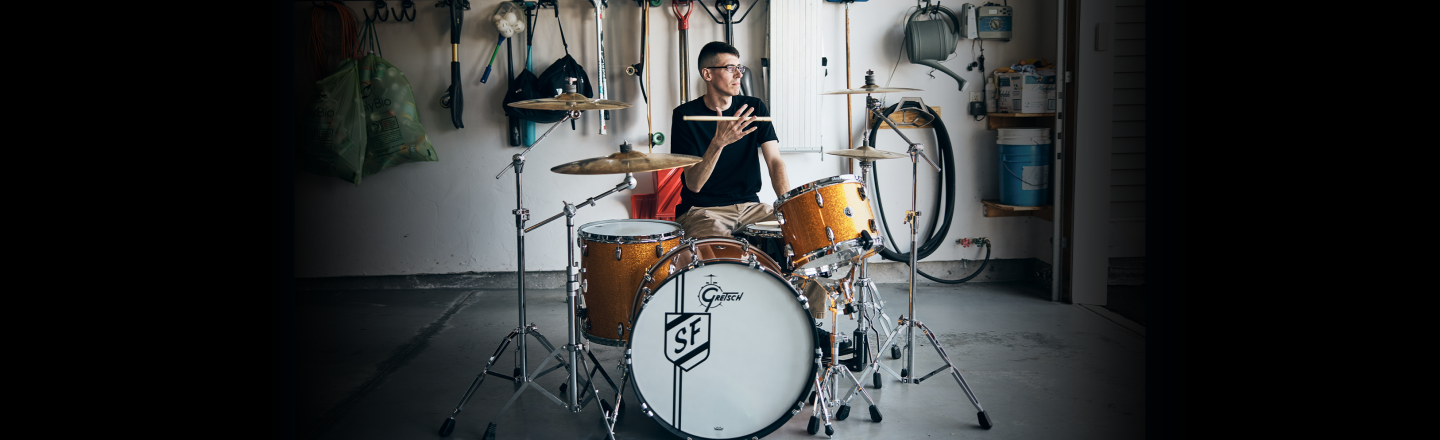 A man plays his drum set in his garage