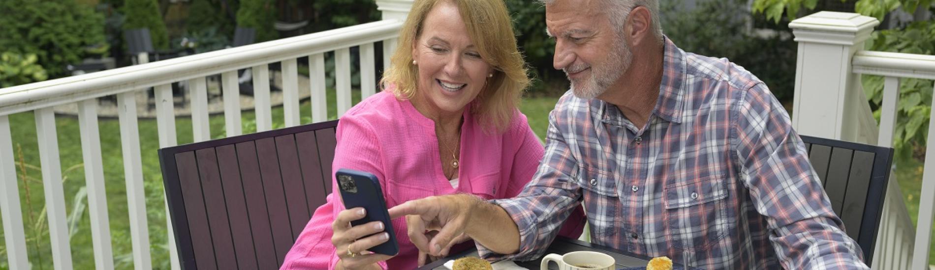 A woman and a man sit at a table and review their bank account on a phone