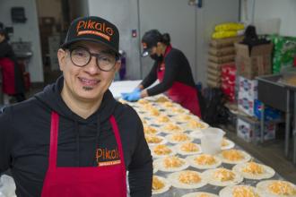 Jose Pimental, owner of Pikalo, stands in kitchen in front of table filled with empanadas