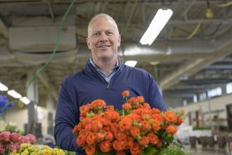 Ted Winston wears a blue sweater and holds a bushel of orange flowers