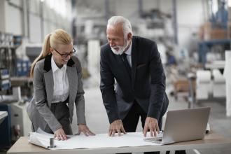 Two business owners review financials on a laptop while visiting the warehouse