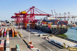 A photography view of a dock in a wharf with a large cargo ship stacked with shipping containers