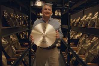 The CEO of Zildjian stands among racks of cymbals and proudly holds one in front of him for the camera