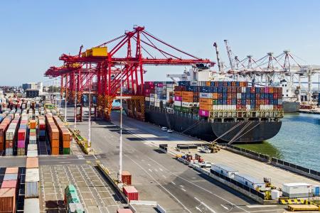 A photography view of a dock in a wharf with a large cargo ship stacked with shipping containers