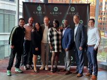 A group of people gather for a picture in front of a backdrop reading Grace by Nia
