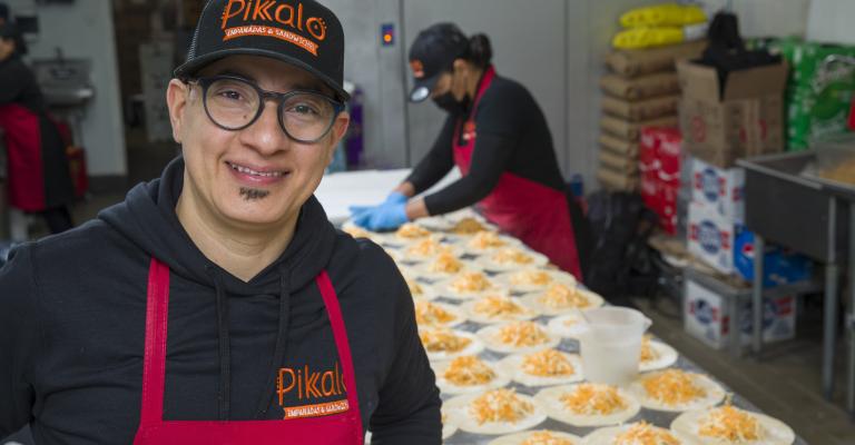 Jose Pimental, owner of Pikalo, stands in kitchen in front of table filled with empanadas