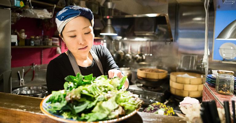 A chef places a plate of salad on the counter for a server to pick up