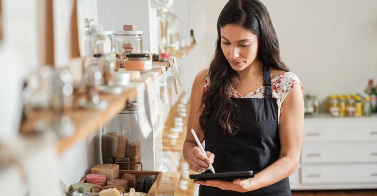 A person stands in their boutique shop and takes inventory of stock on a clip board