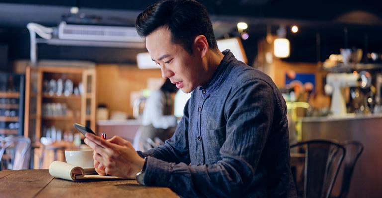 A man sits in a cafe and reviews finances on his phone
