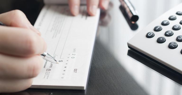 A person writes out a check in a checkbook on top of their desk