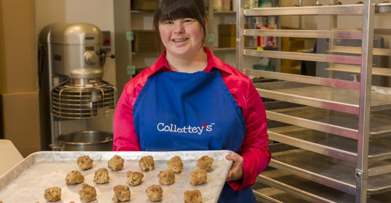 Collette Divitto stands in the kitchen of her bakery holding a tray of cookie dough ready to be baked