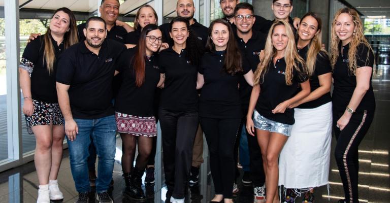 Roads Consulting Group team members stand together in branded black polo shirts and smile at the camera