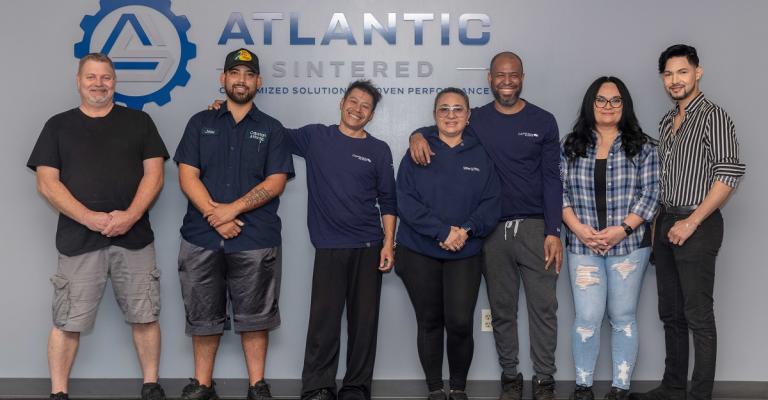 Team leaders of Atlantic Sintered stand together at their office in front of their logo