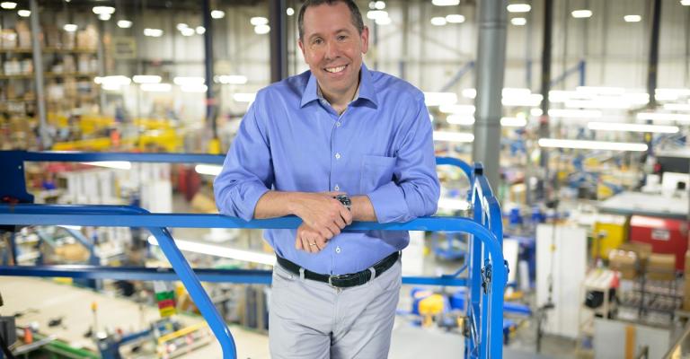A man stands on a lift overlooking his company's supply warehouse