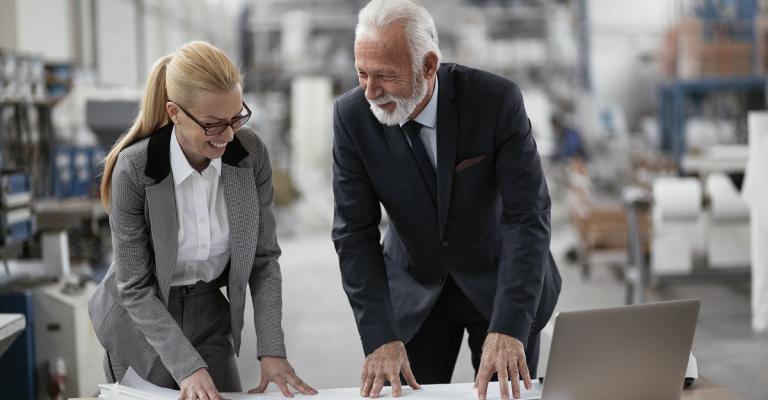 Two business owners review financials on a laptop while visiting the warehouse