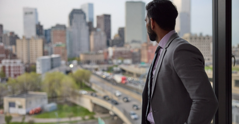 a man wearing a suit stands in front of a glass window looking over the city skyline