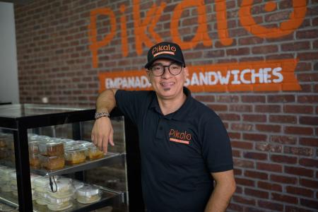 The owner of Pikalo stands by a display of food in his restaurant and smiles at the camera